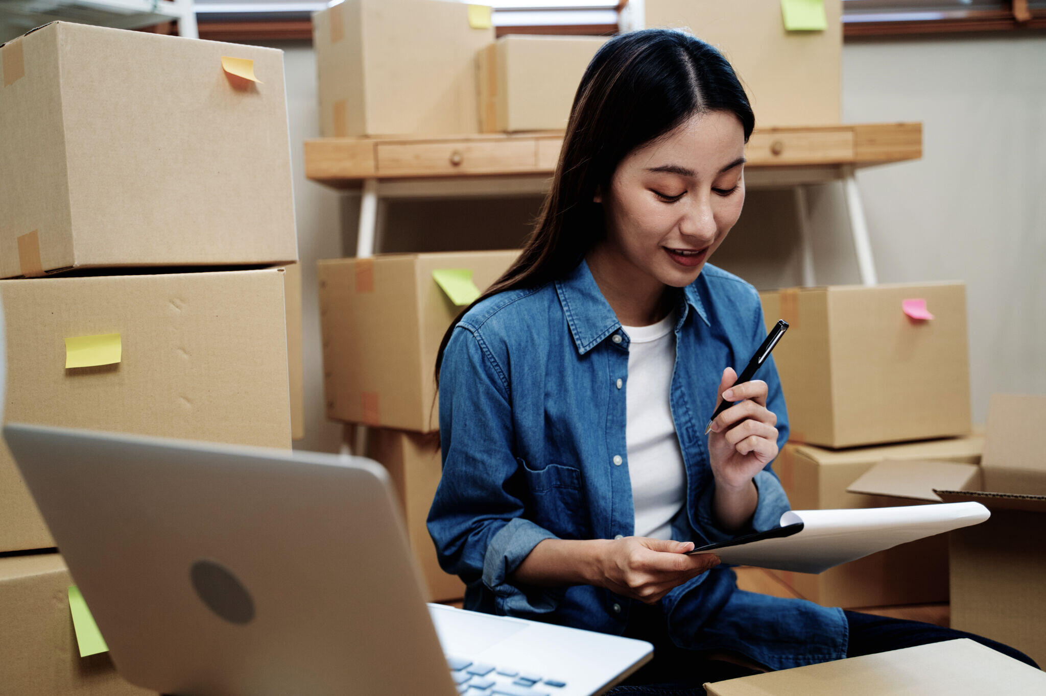 Woman using a tablet and laptop to organize product shipments for an online store.