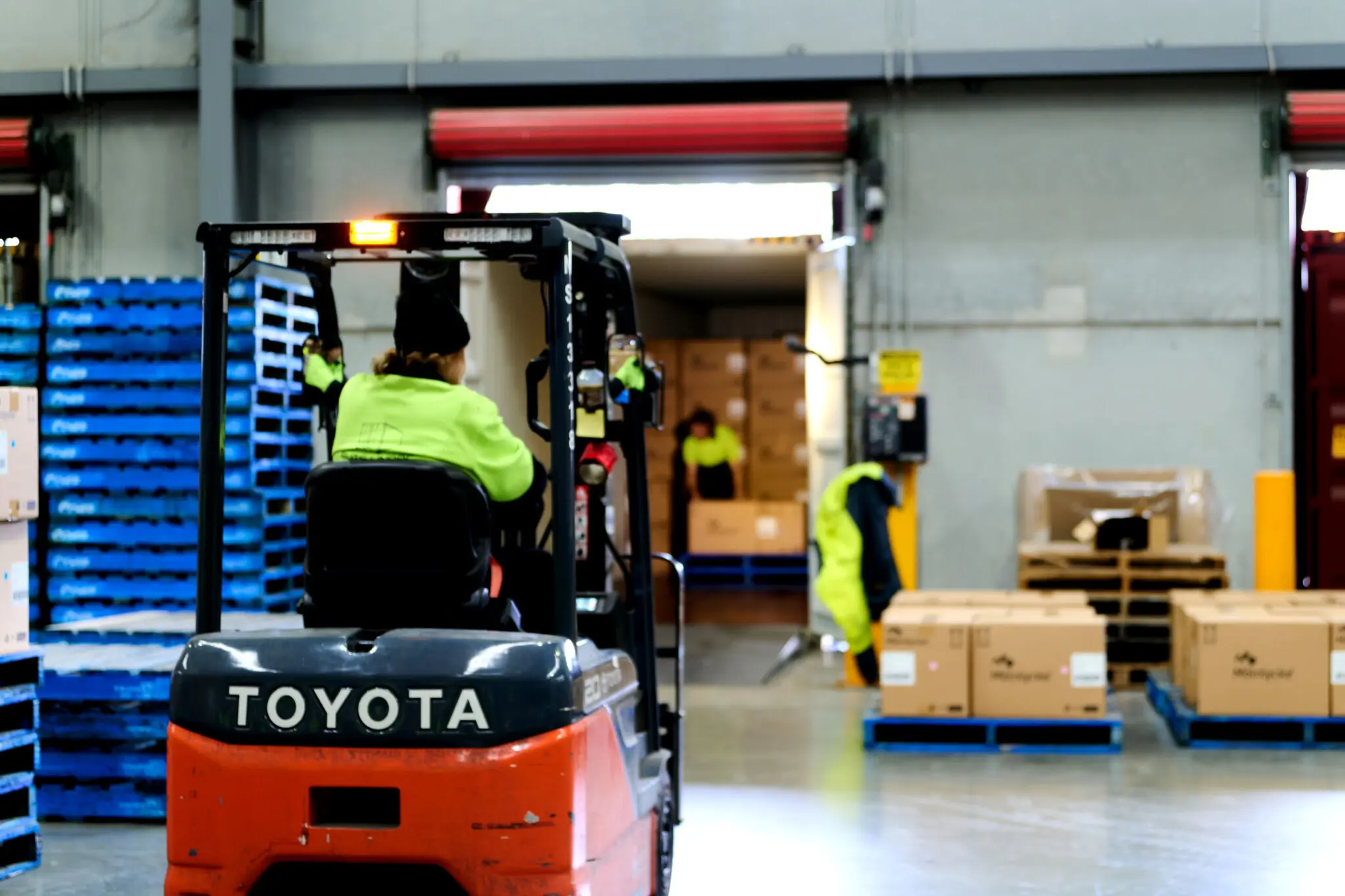 A worker in high-visibility clothing operates a Toyota forklift in a busy logistics warehouse, moving pallets near an open loading dock to illustrate Landmark Global's internal shipping operations in the USA.