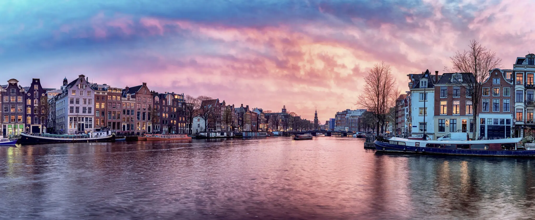 Sunset view of traditional Dutch canal houses and a canal boat in the Netherlands, illustrating Landmark Global's parcel delivery services to the country.