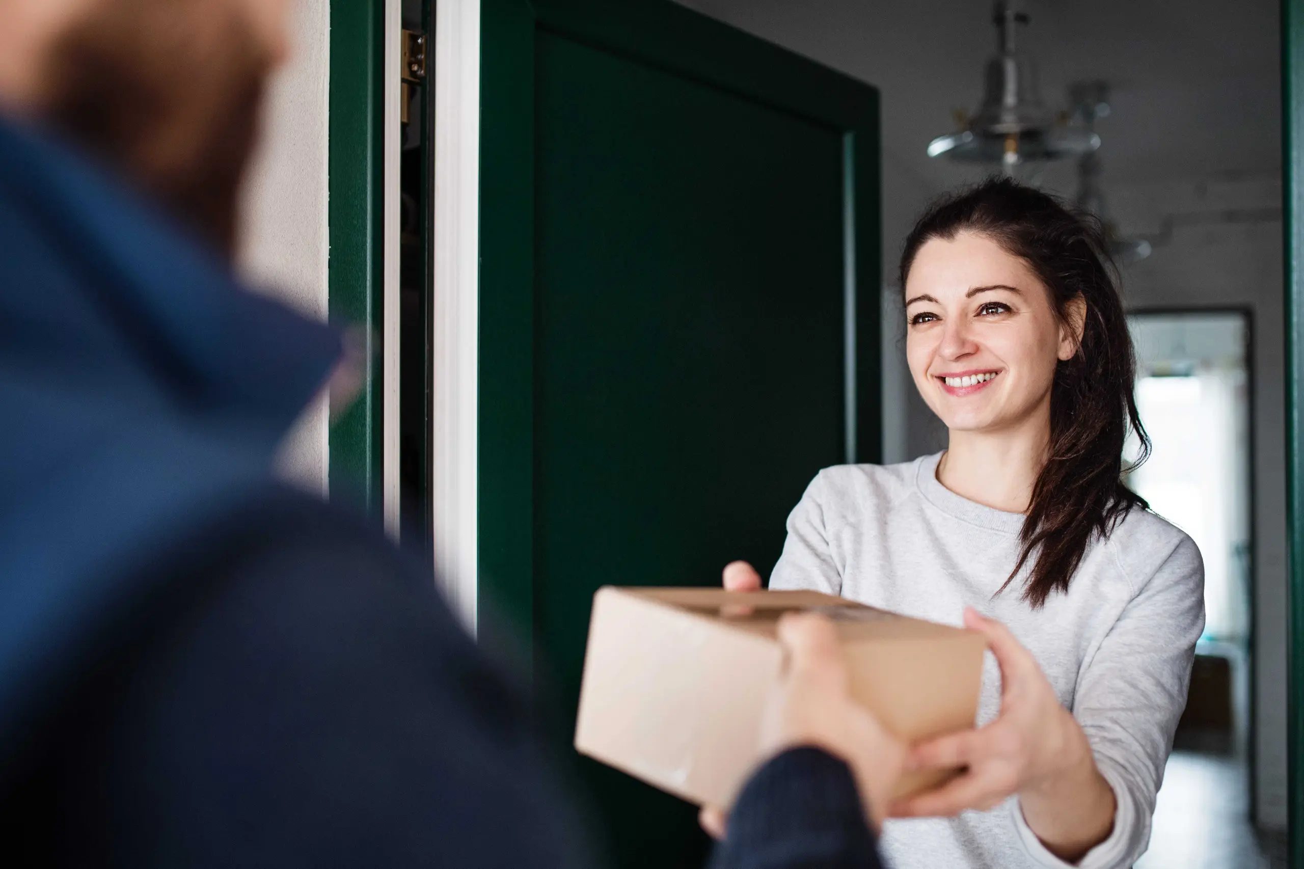 Smiling woman receiving a cardboard parcel at her doorstep, representing Landmark Global's home delivery services in Canada