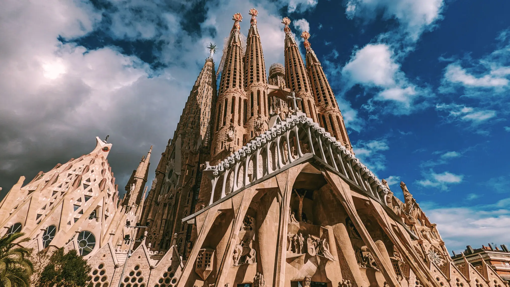 Een close-up van de ingewikkelde architectonische details en torens van de Sagrada Família-basiliek in Barcelona, ​​tegen een blauwe hemel bezaaid met witte wolken, illustreert de bezorgdiensten van Landmark Global naar Spanje.